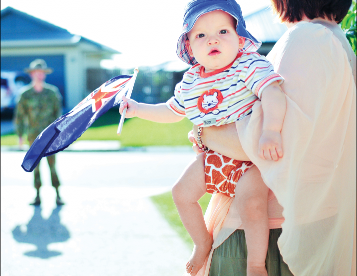Photo: Mother and child welcome home Defence member (Army). Child holds an Australian flag
