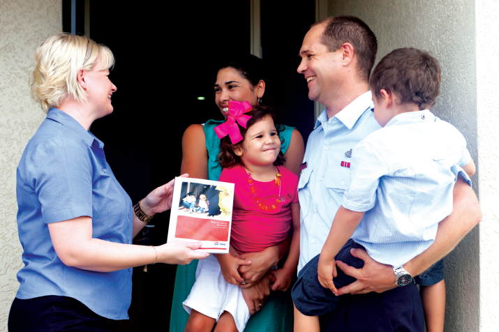 Photo - A DHA Property Manager visits a RAAF family at their DHA home. The staff member presents the family with a Tenant Handbook.