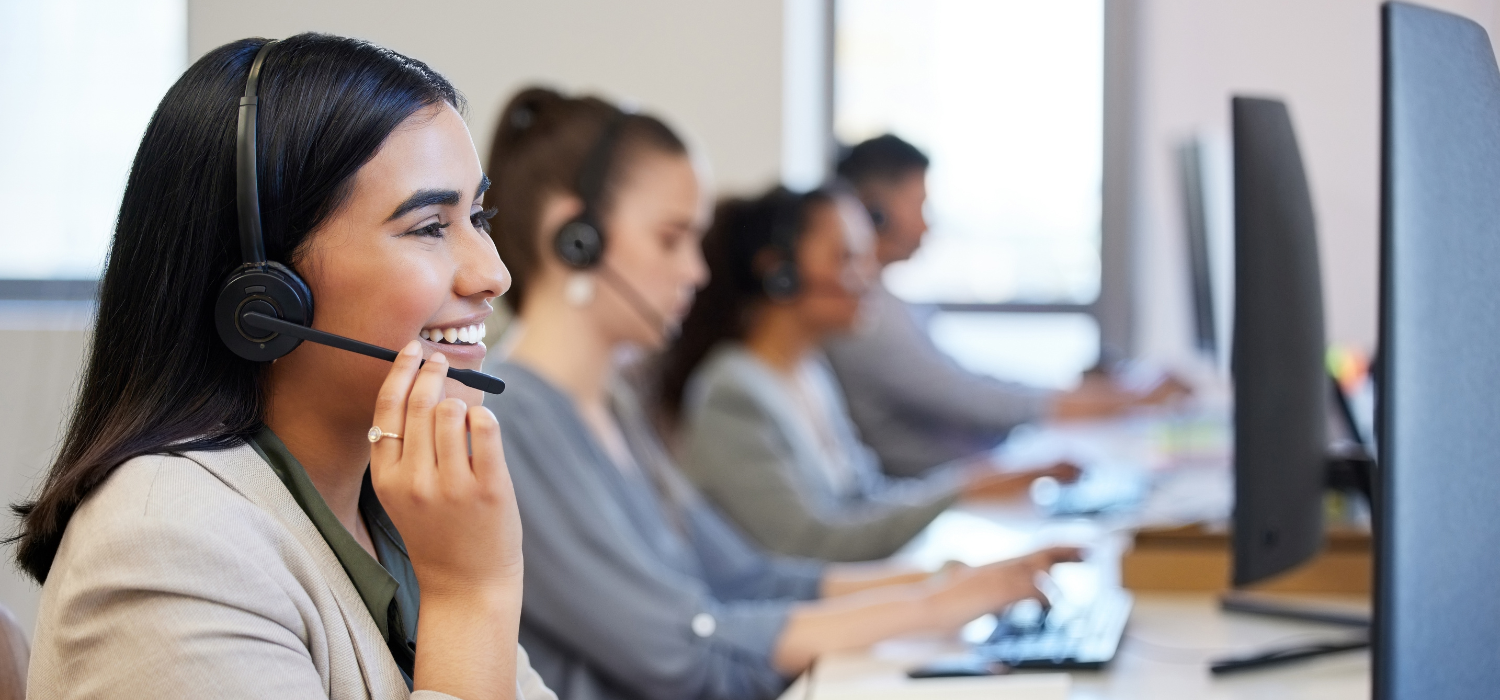 Customer care web banner image of a woman smiling on a headset with other people on headsets in the background